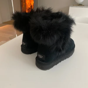 Svarta boots från UGG - Säljer ett par svarta UGG boots med fluffig pälsdetalj runt skaftet. Perfekta för att hålla fötterna varma under kalla dagar. De har en klassisk design med en robust sula. Bra skick andvönt 1 gång ❤️❤️🙌 MAN KAN SKRIVA TILL MIG OM ANNAT PRIS!!