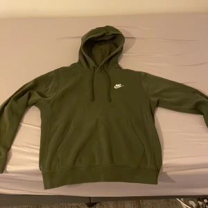 Nike hoodie - Säljer en snygg olivgrön hoodie från Nike med klassisk logga på bröstet. Tröjan har en bekväm passform med långa ärmar och en praktisk magficka. Perfekt för en avslappnad stil.