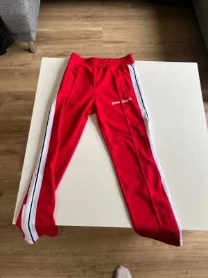 Palm angels track pants - Röda Palm angels track pants i storlek M! Otroligt sköna och väldigt bra kvalite, köpta på farfetch för två månader sedan! Använt dom 3 gånger då jag tycker dom är lite skrikiga i färgen! Helt felfria! Hör av dig vid fler bilder! Mvh 
