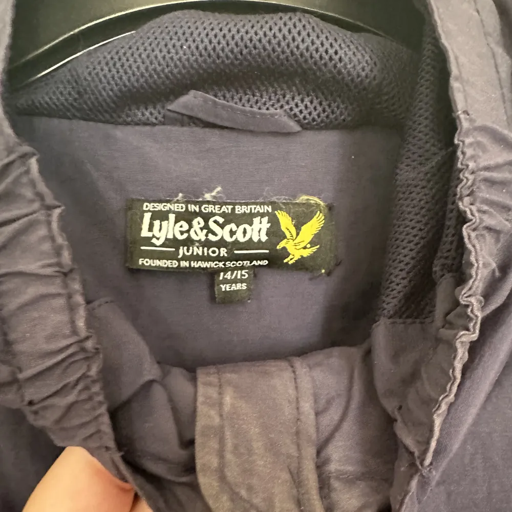 En marinblå vindjacka från Lyle & Scott. Finns lite smink vid kragen, men de går att tvätta bort. Köpt på kidsbrandstore. Storlek 14-15år (Längd 164-170cm. Byst 86-88cm. Midja 75-76cm) (Kidsbrandstores storleksguide) Färg: Navy Blazer. Takit.