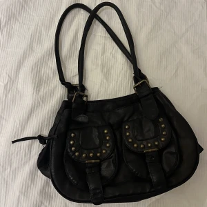 svart väska m nitar  - svart väska jag köpt på 2hand med guldiga nitar, många små & smidiga fack. lite sliten i skinnet (kan skicka bilder) men ändå en väldigt fin och stilren väska! 