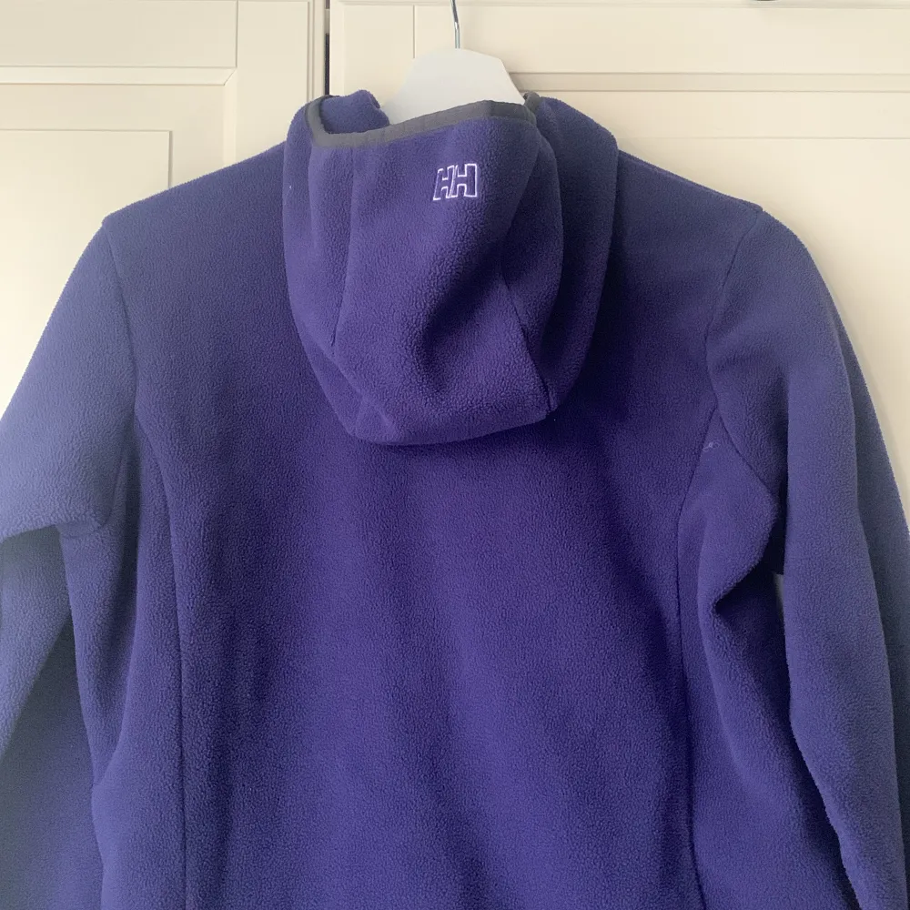 Lila Helly Hansen fleece med två fickor och reflex samt luva. Superfint skick och ej väl använd. . Hoodies.