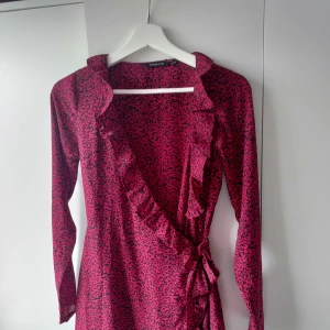 Röd leopardkläning med volanger - Klänning från Ullared, storlek Xs.  Har volanger vid "kjolen" samt halsen även knyte vid ena höften.  Väldigt fin klänning och lite "silkes" material.