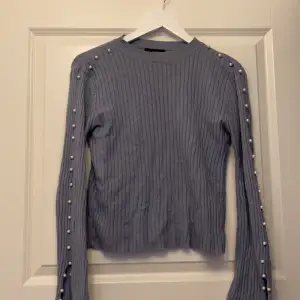 Fin tröja i ljusblå färg, med pärlor längst både ärmarna och slits i slutet på ärmen. Det saknas en pärla