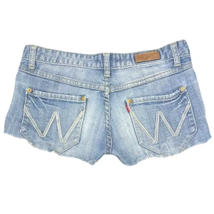 Lågmidjade Vintage Shorts - Du kan köpa varan direkt på vår hemsida, ettmarke.se  Märke: Vintage Modell: Lågmidjade Färg: Blå Storlek: 28 enligt lapp (US). Uppskattad europeisk storlek 38 Midja platt rakt över: 39 cm Totallängd (från midjan): 22 cm Bra skick, få tecken på användning