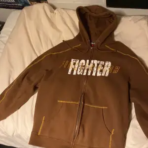 Snygg brun fighter gear zip-up hoodie med snygg gul stitching. Size xl men skulle säga att den sitter mer som size M