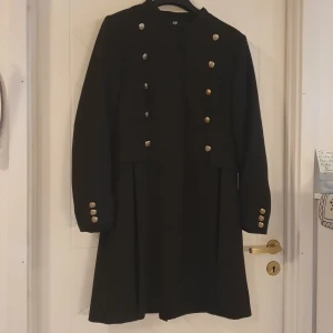 Mörkgrön kappa - Mörkgrön kappa från H&M. Storlek 44 men känns som en storlek 42. Knappar fram, bak + manschettknappar.  Aldrig använd. Känns lite retro. 