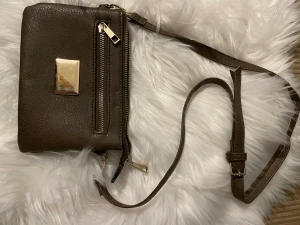 Brun liten väska - En liten brun väska med guld detaljer, alla dragkedjor funkar. Är mycket använd och det syns även på väskan. Den är ej trasig men tecken på användning finns