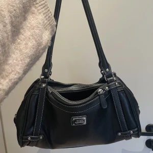 Svart väska - En svart liten/medel handväska i svart ”läder/skinn”. Silvriga detaljer och väldigt rymlig med många fickor inuti. Knappt använd, fint skick. Osäker på märke då den är köpt här på plick.