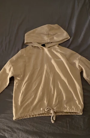 Hoodie - En beige hoodie med knytband vid midjan. Det står ”Dreamer” på vänstra sidan. Använt ett par gånger. Köpt för ca 2 år sedan. 