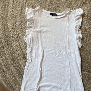 Volang linne/t-shirt - Säljer denna fina vita t-shirt/linne med volang. Köpt på new yorker. Är i storlek xxs men skulle säga att den passar xs också🫶🏼