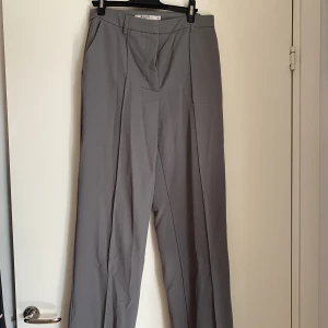 Gråa kostymbyxor  - Gråa kostymbyxor från NA-KD, slits vid foten. Väldigt fin passform. En liten fläck på ena knät (se bild), syns knappt när man har dem på sig 