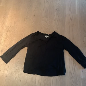 Svart Blus - En jättefin svart blus med små volanger vid erm kanten och kring halsen.Saknas en liten knapp men syns knappt❤️