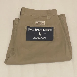 Oanvända Ralph Lauren Chinos - Ett par oanvända Ralph Lauren chinos i amerikansk storlek 14 (i svensk storlek blir det 146-152). Färgen är klassisk chinos-beige ✨