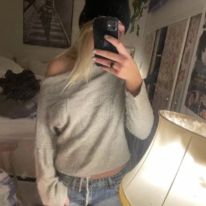 Grå stickad - Unik grå stickad tröja med ficka på framsidan. Urringningen är bred så den går att ha off shoulder eller på en axel. Längst ner kan man knyta tröjan för att kunna spänna den och göra den kortare. 
