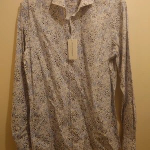 Ny Bruun & Stengade skjorta slimfit  - Helt ny kvalitets skjorta från välkända danska design företaget Bruun & Stengade , ljusblå blommigt mönster i Slim fit och easy care , det vill säga att behövs ej strykas. Orginal tags och prislapp på 800kr är kvar.  Mitt pris: 199 kr plus frakt 50 kr 