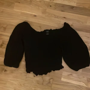 Svart ribbad topp - Storlek S från Lindex. Svart och har ribbat mönster runt ryggen och magen. Vanligt slät tyg vid armarna. Tunt tyg. Toppen slutar ungefär vid naveln där nånstans. Fyrkants form vid halsen och nacken.
