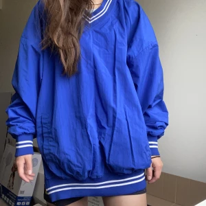 Windbreaker tröja  - Ny windbreaker jacket, testad 2 ggr. Har en dragkedja på vänster sida. Mudd vid ärmar och vid fållen. Har 2 fickor! Köpte den för att använda som Oversized.   Jättesnygg vibrant färg.  Köpte för 700 kr. Märke: Russel  Ger en känsla som amerikansk fotboll