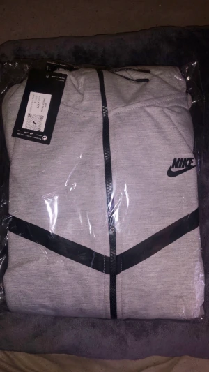 Grå Nike tech kofta  - Grå Nike tech kofta storlek L precis som den originella helt ny i paket. Den säljs billigt komplett med både kofta och byxor.