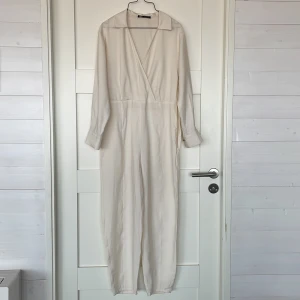 Byxdress från zara - Säljer denna vita v-ringade byxdress från zara i storlek xs men skulle säga att den också passar s💕Har dragkedja i sidan och har även hällor för skärp.