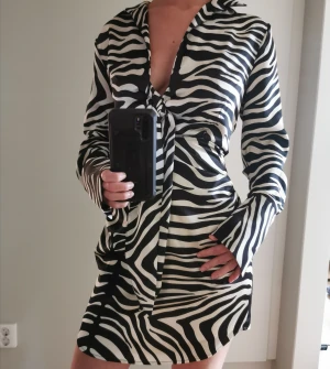 Mönstrad klänning  - Zebramönstrad långärmad klänning som slutar strax ovanför knäna. Krage, knytdetalj framtill, löst sittande.  Nyskick - aldrig använd. Prislapp kvar. Ord. Pris 699.  Storlek 34/XS