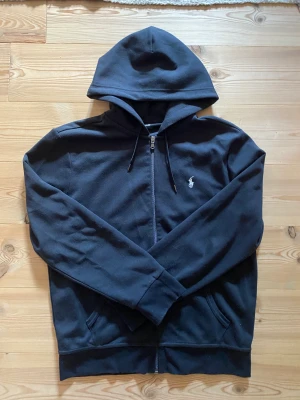 Polo Ralph Lauren zip hoodie - Hej, säljer en fin men använd zip hoodie från Polo Ralph Lauren.  Zip Hoodien är svart (ljuset gör att den ser lite mer blå ut), samt storlek M och väldigt fin för att vara använd. Det finns inga hål eller skador på tröjan men är i använt skick.