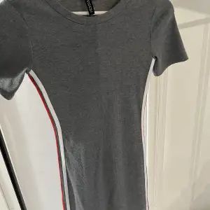 Denna gråa klänning är köpt för ca 150kr på H&M för några år sedan. Den är lite kroppsformad men inget jag använder längre. Den är ribbad med vita och röda detaljer på vardera sida av klänningen. Simpel o söt💗