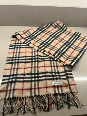 Burberry halsduk - Burberry halsduk. Sparsamt använd. 50% cashmere 50% wool. Mått 170 cm lång 30 cm bred. Kommer från rök och djurfritthem