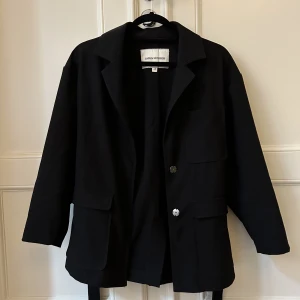 Carin Wester Tunn jacka / kavaj - Ofodrad svart ”knytkavaj” / tunn jacka med fickor från Carin Wester. Tyget har blivit lite nopprigt på vissa ställen men inget man lägger märke till.  