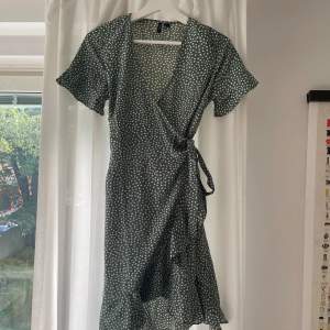 Gröngrå knälång klänning med prickar. Omlott-modell med knyte, volanger längs armar och nederkant. Använd vid 2-3 tillfällen! 