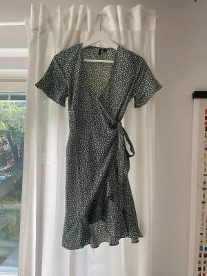 Gröngrå knälång klänning med prickar. Omlott-modell med knyte, volanger längs armar och nederkant. Använd vid 2-3 tillfällen! 