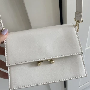 Vit axelremsväska med gulddetaljer - Vit axelremsväska med gulddetaljer säljes🤍