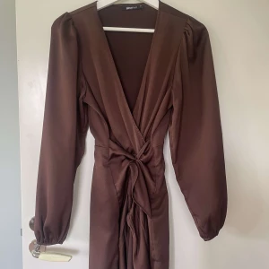 Klänning  - Brun klänning från ginatricot. Vacker knytning, klänningen har ett fint fall och långa ärmar. Storlek S, passar XS. 