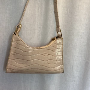 Beige handväska - Beige handväska i snakeprint. Har några svarta märken på undersidan men syns inte vid användning. Väl använd. 