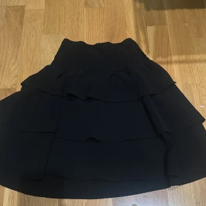 Svart kjol  - Säljer en snygg svart kjol med volanger. Den är figurnära upptill och ger en riktigt snygg look!