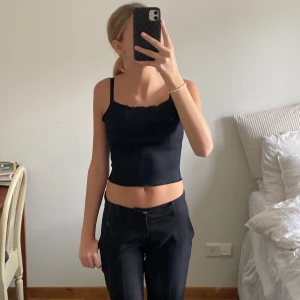 Svart ribbat linne  - Ett svart ribbat linne med lite volang högst upp, det är även spänn bara band! Köpt på bikbok 