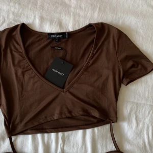 Croppad top med knytning - Brun top med knytning i jättemjukt och stretchigt material. Banden går att knyta på flera sätt och den sitter jättebra när man knutit den. Endast testad så helt ny med prislapp kvar! 