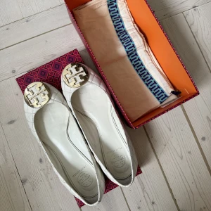 Tory burch ballerinaskor! - Sparsamt använda ballerinaskor från Tory Burch. Vitt läder med gulddetalj, låda och dustbag medföljer🤍✨Nypris 2999kr, mitt pris 500kr!