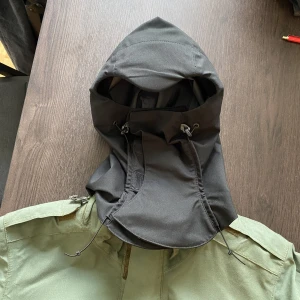 Militär Balacava jacka - En unik regnjacka gjord för den brittiska miltitären av leverantören RFD Beaufort. Har massa sjuka detaljer och en ihopfällbar luva, som också agerar som en balaclava. Helt oanvänd. Sitter som en cropped storlek M. 