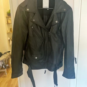 Skinnjacka J Lindeberg stl 40 - Hej! Säljer min helt oanvända skinnjacka i mjuk lambsnappa från JLindeberg i bikermodell. Den är i storlek 40, normal i storleken. Mjuk och bekväm. Flertalet fickor både med dragkedja och knapp, samt bälte med spänne.  