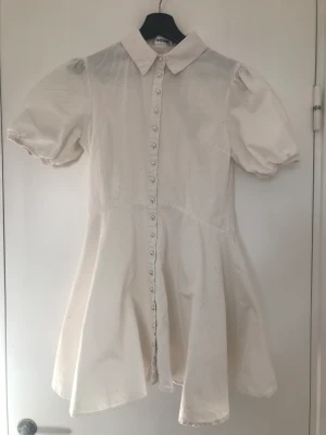 Vit skjortklänning med puffärmar - Söt vit akjortklänning med puffärmar, vid kjol och pärlknappar från Missguided. Aldrig använd endast provad.  Stl XS/34