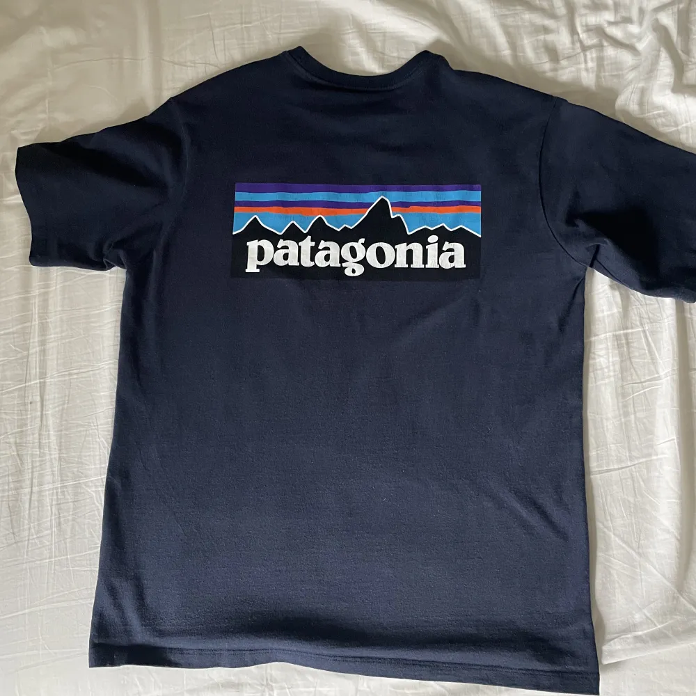 En mörkblå t-shirt från Patagonia. Den är i bra skick men trycket där bak har flagnat lite men ingen risk att det trillar av. Nypris 499kr. Storlek M. Jag är 187 lång.. T-shirts.