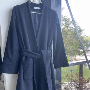 Mörkblå kappa med skärp i midjan från Stylein. Storlek S, 80% ull, 20% polyester.