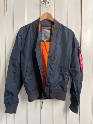 Alpha Industries bomberjacka - NYTT PRIS! Marinblå bomberjacka med orange foder från Alpha Industries. Något blekt halsmudd och armmudd. Annars i fint skick.  Storlek Medium men väldigt liten i storlek. Använd av 12-14-åring 