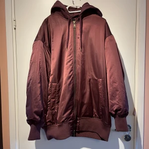 Oversize Vinröd Bomberjacka Urban Outfitters - Vinröd bomberjacka i satin-material. Lite längre modell, väldigt oversize! Avtagbar luva i hoodiematerial.  Storleken är S, men skulle säga att den mer är som en M. Jag kunde även ha den förut när jag hade en mindre L som storlek! 🌸 Nypris: 1190 kr