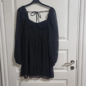 Svart kortklänning - Svart klänning med långa armar. Har en drqgkedja på sidan och rosett i ryggen. Når till mitten av låren.