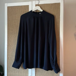 Mörkblå Blus - Fin blus från Carin Wester, mörkblå med lite ’textur’ se bil 2. Två knappar bak i nacken, se bild 3.  Knappt använd 