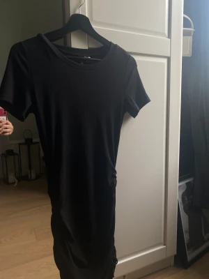 Klänning - Svart ribbad klänning som har korta armar. Klänningen är ribbad på båda sidorna för framhäva formerna