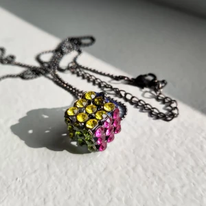 Halsband med Rubiks kub - Jättefint halsband med en berlock som liknar en Rubiks kub! Mycket bra skick då den aldrig använts. Kedjan är ca 46 cm lång och berlocken är ca 1,5 x 1,5 cm. 