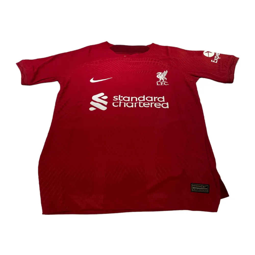 En Liverpool tröja i storlek s som är röd. Den är perfekt passande och av hög kvalitet. Dess andningsförmåga gör den idealisk för både matcher och träning.. T-shirts.